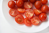Fresh red fruits of small tomatoes on a glass plate. Juicy chopped cherry tomatoes.