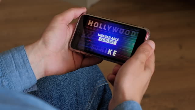 Blue Warning News about Hollywood Strike on Smartphone Screen in male hand