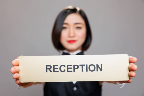Professional asian waitress holding in hands tabletop reception plate portrait. Restaurant woman administrator in uniform showing receptionist steel signage and looking at camera