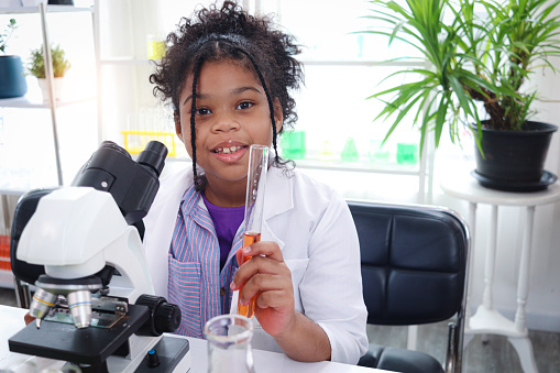 Primary school African curly hair girl does chemistry science experiment in laboratory, cute scientist kid holds chemical test tubes, child use lab equipment to learn biologics, chemistry in classroom