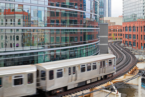 Chicago cityscape featuring a commuter train traveling on the elevated tracks of the Chicago “L” train system as it curves between the buildings of the downtown district.