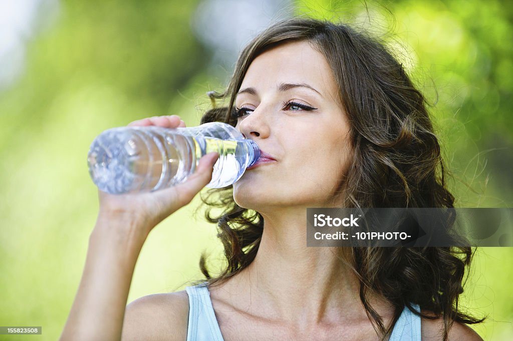 young dark-haired woman drinking water Portrait of young beautiful dark-haired woman wearing blue t-shirt drinking water at summer green park. Women Stock Photo