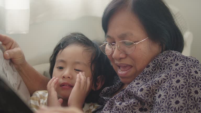 Asian senior woman dressed comfortably grandmother and grandson with  she is lying at home reading a story in living room.