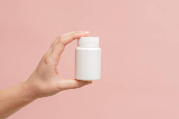 istock White bottle (plastic tube) in hand on pink background. Packaging for vitamins, pill or capsule, or supplement. Mockup for product branding 1558259446