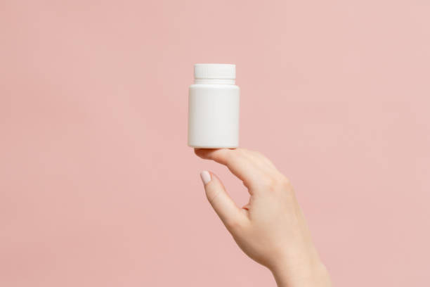 istock Plastic bottle (tube) in hand on pink background. Packaging for vitamins, tablets or capsule, or supplement 1558259463
