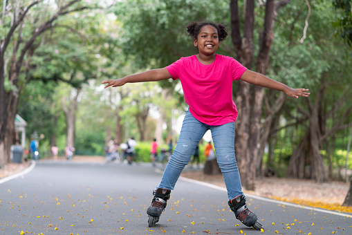 Happy African American girl playing roller skate on road in park.Sport outdoor for kid.