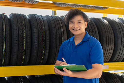 Portrait of Asian male technician worker checking new tires wheel on shelf at auto store shop and car repair service