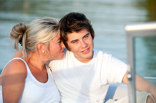 A closeup head and shoulders image of a smiling  real mother and son. The image is outdoors on a sunny day in a wakeboard on lake.