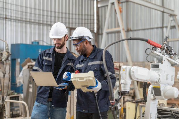 istock Male engineers wearing vest with helmet safety using laptop and remote controller control inspection robot arm welding machine in factory. Team of technician automation robot system. 1558301598