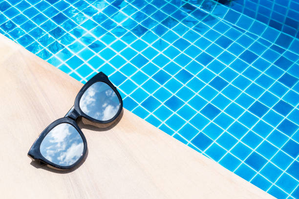 istock Sunglasses on swimming pool edge with space on blue water background 1558305435