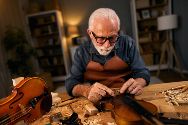 falegname senior artigiano che intaglia il legno e costruisce strumenti di violino - workshop old fashioned old instrument maker foto e immagini stock