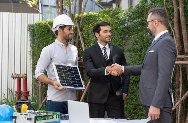 istock Electrical engineer with businessman handshake agreement project installation solar cell panel on the roof of building. Alternative energy concept. 1558330353
