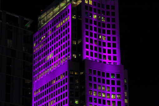 Brickell World Plaza lit up purple at night in downtown Brickell in April. The tower is rectangular in shape with countless square windows. The tower is in the heart of Brickell Miami and is a iconic building due to its age and being lit up