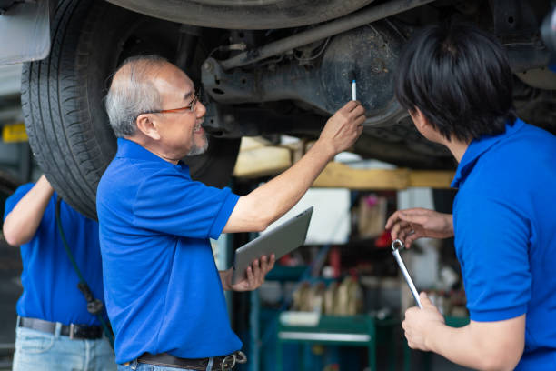 ingeniero asiático superior que enseña a los trabajadores de reparación y mantenimiento del eje trasero del automóvil. técnico de grupo en uniformidad revisando y dando servicio a vehículos en garaje. - auto repair shop mechanic digital tablet customer fotografías e imágenes de stock