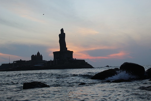 The iconic Thiruvalluvar Statue at sunset in Kanyakumari, India, with a beautiful orange sky