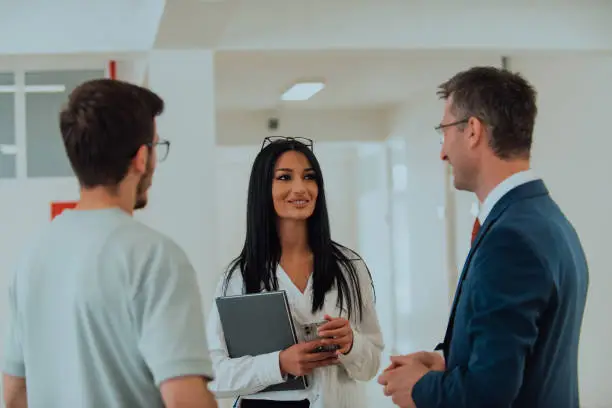 Photo of The director conducts a conversation with the secretary and a young programmer in a modern and spacious corridor of a large company, discussing various business topics and projects.