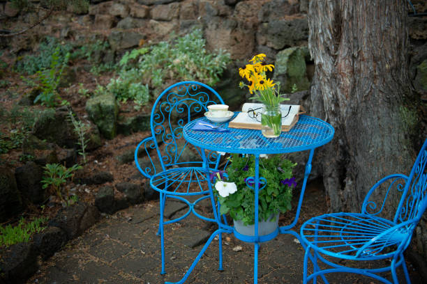 Blue table and chair with open book and tea cup. Flowers under the table. Small patio setting