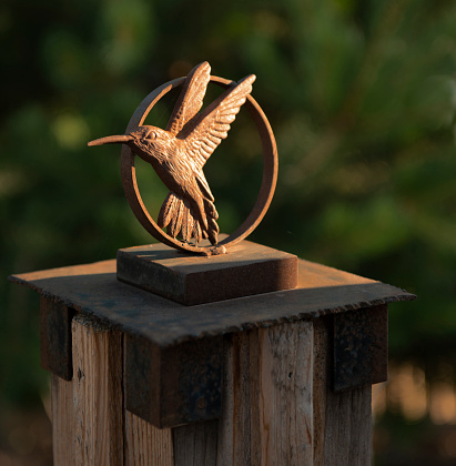 A close-up view of a metal sculpture of a steel ring with a welded stamped hummingbird symbol attached. Side lighting accentuates the bird detail.
