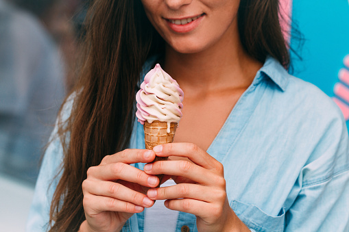 Young woman eating refreshing sweet ice cream cone in summer hot weather near ice cream shop
