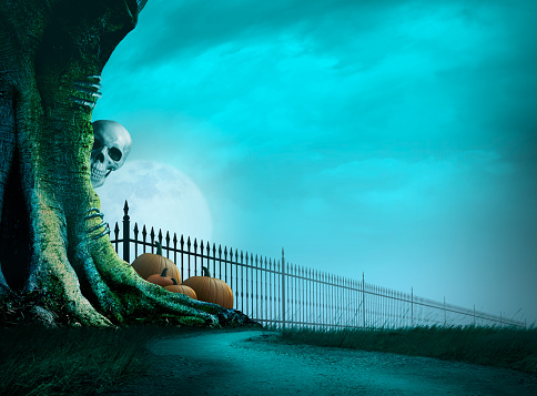A skeleton peeks out from behind a gnarled tree along a dirt footpath that parallels along a wrought iron fence. A full moon rises in the distance on Halloween night.