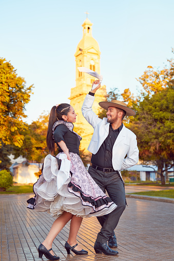 full body portrait young adult latin american couple dancing cueca traditional dance with huaso dress in the city square of La Serena