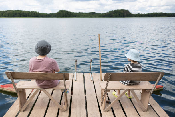 Two teenage boys in hats sitting on benche on the pier near lake.