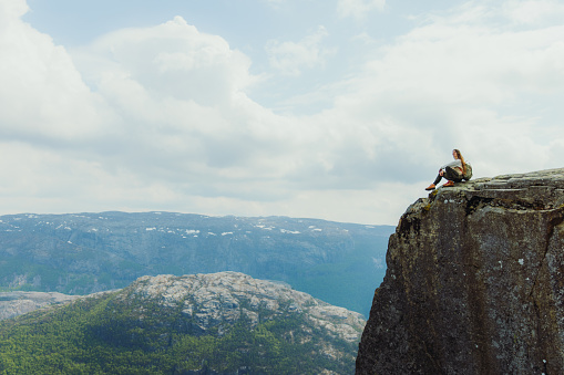 Side view of female hiker getting to the edge of the cliff admiring scenic view of Lysefjord in South Norway, Scandinavia