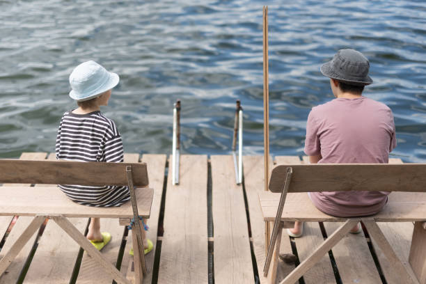istock Two boys sitting on a pier near lake 1558431347