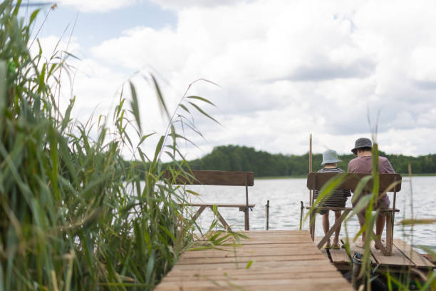 istock Two boys sitting on a pier near lake 1558432431