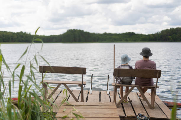 istock Two boys sitting on a pier near lake 1558432434