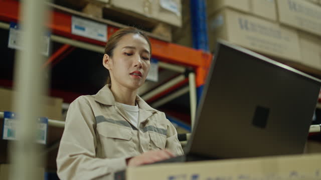 Asian Warehouse woman or factory worker with uniform stand between shelves in workplace.Concept of good management and happiness of staff during work in industrial business.