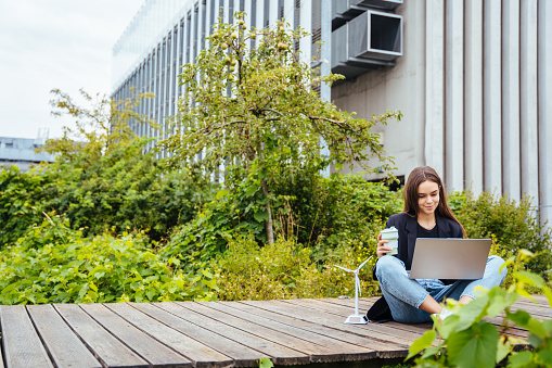 Hardworking inventive woman developing her engineering project, having coffee to go outdoor in modern roof of modern office building. Renewable energy concept. Project presentation work.