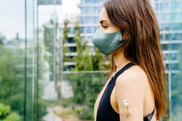 istock Vaccinated woman in mask having patch with flower on shoulder. 1558568269