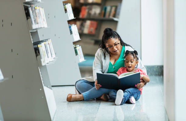 menina mestiça lendo com a mãe na biblioteca - picture book library preschool bookshelf - fotografias e filmes do acervo