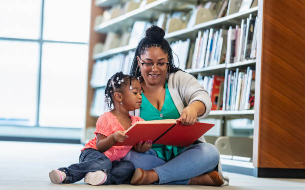 Mixed race little girl reading with mother in library