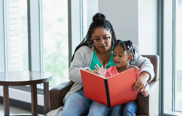 istock Multiracial girl sitting with mother, reading book 1558586805