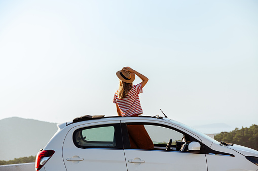 Portrait of a young woman looking at the view from the open roof of her car