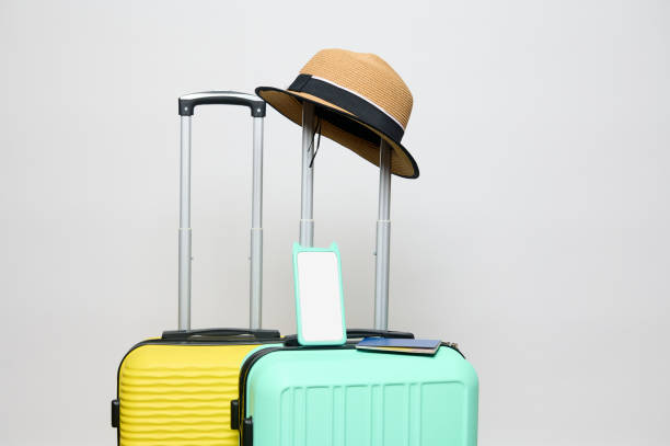 istock Straw hat on handle of a light green suitcase and modern smartphone with white blank digital screen, isolated background 1558739431