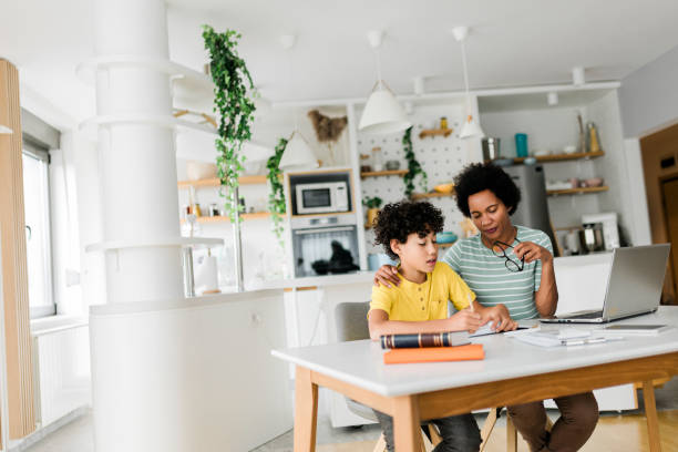 istock Boy writing on a book while his mother working on laptop. Kid studying with mother working from home. 1558807407