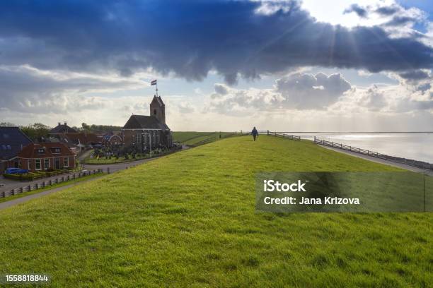 Holland Hindeloopen Coast High Coastal Wall Overgrown With Grass On The Right Side Of The Sea And On The Left Side Houses Hindeloopen And A Wooden Church Dramatic Sky With Clouds Stock Photo - Download Image Now