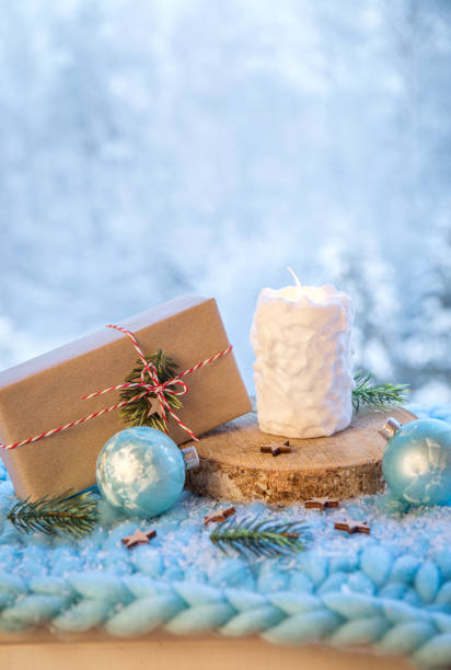 contexte des produits de noël. bougie blanche à motif boule de neige allumée, cadeau de noël enveloppé dans du papier brun avec ficelle blanche et rouge sur disque en bois avec fond forestier d’hiver enneigé bokeh. - wrapped package string box photos et images de collection