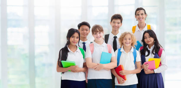 Group of cheerful latin high school students wearing a white uniform shirt and carrying backpacks standing in school hallway