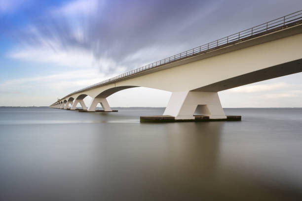 istock Zeeland Bridge - long white bridge over the river, beautiful blue sky with dynamic clouds. Long time, calm water of the Oosterschelde .. 1558826116
