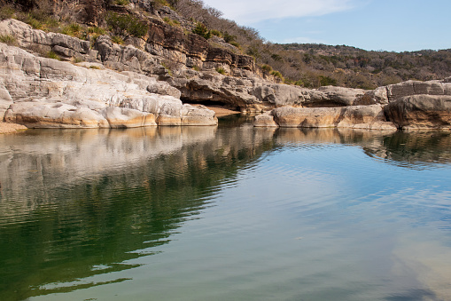 A wall of geological limestone formations creates a canyon and cliff overhang near the river in Pedernales Falls State Park as part of the Texas Hill Country