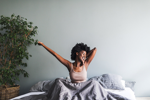 Young black woman waking up and stretching in minimalist grey modern bedroom