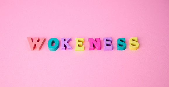 the word wokeness laid with colorful wooden letters on pink background