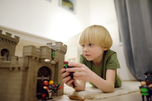 Little child is playing with toy prototype Medieval Castle. Knights and battles - favorite game for boys. Entertainment for kids indoors. Offline games.