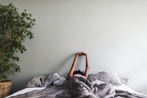 Young black woman waking up and stretching in minimalist grey modern bedroom