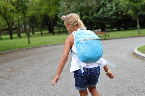 Pupil girl child with backpack going to school on the street