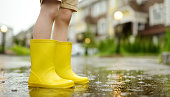 Little boy wearing yellow rubber boots walking on rainy summer day in small town. Child having fun. Outdoors games for children in rain.